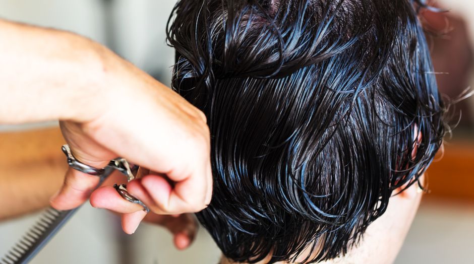 Close-up de um cabeleireiro cortando cabelo molhado e escuro com tesouras em um salão.