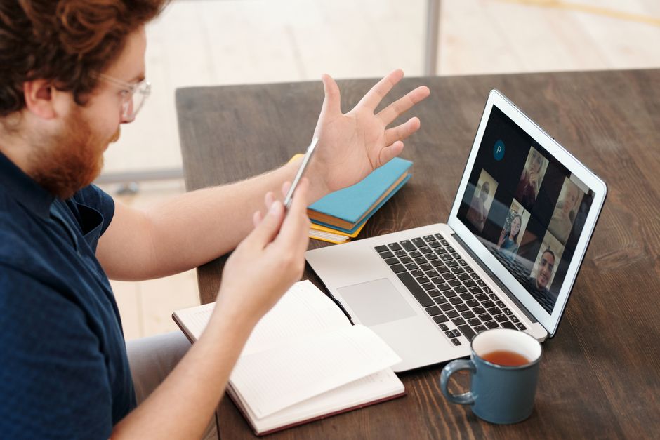 Homem participando de uma reunião virtual em casa com laptop e chá, conversando e estudando online.