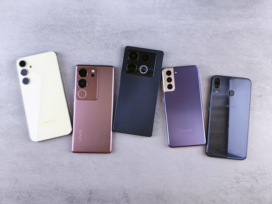 Vista de cima de cinco smartphones modernos em uma superfície cinza, exibindo vários designs.