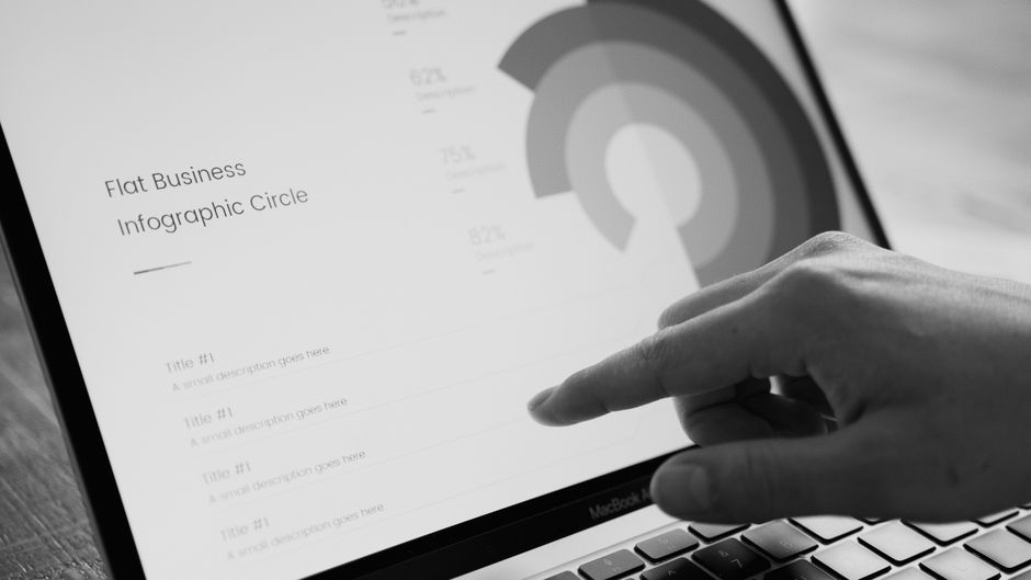 Dedo apontando para um círculo de infográfico de negócios na tela do laptop em tons de cinza.