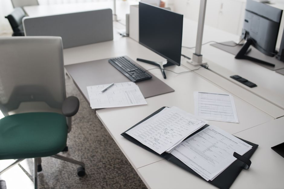 Uma mesa de escritório limpa e organizada com documentos, um computador e uma cadeira em um ambiente de trabalho moderno.