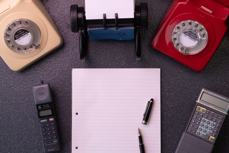 Equipamento de escritório vintage com telefones de discagem, caderno e calculadora dispostos em plano horizontal.